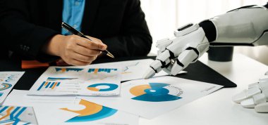 İnsan bir profesyonel, modern ofis ortamında, iş verimliliğini ve yeniliğini artırmak için veri tabloları ve raporları analiz ederek robotik bir el ile iş birliği yapar.