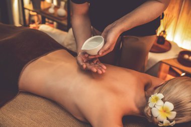 Masör elleri kadının sırtına aroma yağı döküyor. Masözler lüks otellerdeki kaplıca salonundaki müşteriler için yağ masajı prosedürü hazırlıyorlar. Aroma yağı vücut masajı konsepti. Sessiz.