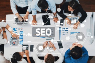 Diz üstü bilgisayarlar ve görsel veri analizleriyle bir SEO stratejisi üzerinde çalışan bir ekibin kuş bakışı görüntüsü. Set, dijital pazarlamada yenilikçiliği ve etkili planlamayı teşvik ediyor. Dostluk