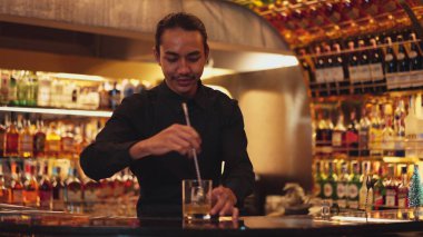 Zeki Asyalı barmen, bardakta karıştırılmış alkol şurubunu buzla karıştırıyor. Lüks gece kulübünde gece hayatı karışımı sergilenen özel bir içecek. Vinosity.