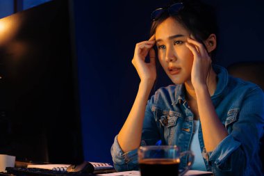 Stresli, genç, güzel Asyalı yaratıcı proje yaratıcısı sosyal medyayı araştırmak için bilgisayara bakıyor ve geceleri daha çok neon modern ofisin planlama kanalı stratejisine ulaşılıyor. Taktik.