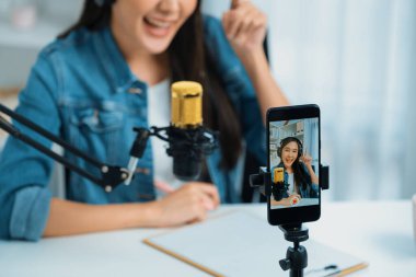 Asyalı sunucu canlı yayında canlı yayında canlı yayında sosyal medyada kulaklık takarak konuşuyor. Dinleyicileri modern stüdyoda koçluk yaparak selamlıyor. Taktik.