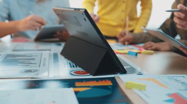 Değişik bir ekibin, veri görselleştirmeleri ve grafiklerini gösteren dijital bir tabletin yer aldığı, bir masanın etrafında ortak bir tartışmaya girişini gösteren dinamik bir ofis sahnesi. SACTR