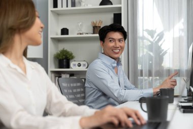Gülümseyen Asyalı bir adam, yan görüntüdeki modern ofis çalışma masasında veri tabanını ararken günlük dizüstü bilgisayarla pazarlama raporu projesini planlarken kadın meslektaşıyla konuşuyor. İnfobahn.