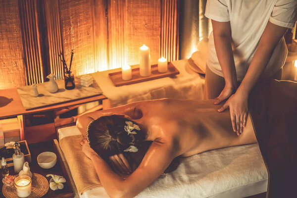 Caucasian woman customer enjoying relaxing anti-stress spa massage and pampering with beauty skin recreation leisure in warm candle lighting ambient salon spa at luxury resort or hotel. Quiescent