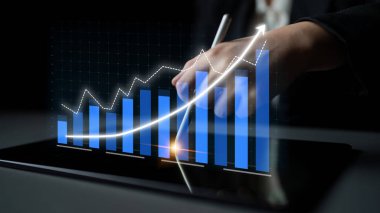 Bir iş adamı tabletteki dijital finansal verileri yakından inceler. Canlı tablo büyümeyi gösteriyor ve pazar eğilimleri ve başarı hakkında içgörü sağlıyor. Etki