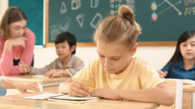 Stresli öğrenci, sınıfta çok kültürlü çocuklar yazarken ya da soruları cevaplarken tahtada otururken test yapmaya odaklanıyor. Becerikli öğretmen sınıf çalışmasını açıklıyor. Pedagoji.