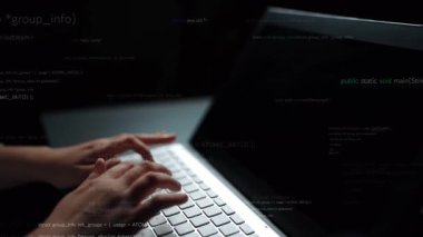 Dizüstü bilgisayarın klavyesine yazılan ellerin yakın plan görüntüsü. Değişen kod satırları arasında, karanlık bir ortamda programlamanın ve modern teknolojinin özünü gösteriyor. Xenic