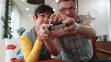 Büyükbaba ve torun birlikte konsol oyunu, eğlence medyası oynuyorlar. Eski kullanım teknolojisi yeni nesil ile iletişim kurar. Nesiller arası uçurum aile bağını güçlendirir. Uyumsuzluk.