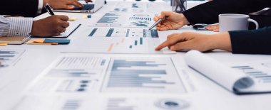 Modern bir ofis ortamında tablo üzerinde grafikler ve grafiklerle veri analizi yapan dinamik bir iş toplantısı. SACTR