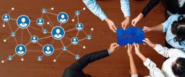 Modern ofis ortamında takım çalışması ve bağlantıyı sembolize eden mavi bir bulmacayı bir araya getirirken, çeşitli profesyonellerin işbirliği içinde ağ kurdukları ilgi çekici bir sahne. Dostluk