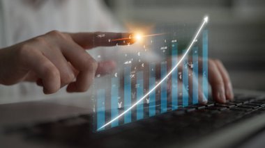 İş dünyasından bir profesyonel, dijital bir grafikle dizüstü bilgisayarda etkileşime geçerek, artan bir ölçü eğilimi sergiliyor, finans alanında büyüme ve veri analizini temsil ediyor. Etki