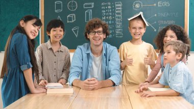 Profesyonel Kafkas öğretmeni ve çeşitli öğrenciler kameraya bakarken mutlu çocuk başparmak gösteriyor. Sınıfın önünde dururken gülümseyen bir grup çok kültürlü çocuk. Eğitim. Pedagoji.