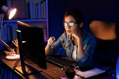 Stresli, genç, güzel Asyalı yaratıcı proje yaratıcısı sosyal medyayı araştırmak için bilgisayara bakıyor ve geceleri daha çok neon modern ofisin planlama kanalı stratejisine ulaşılıyor. Taktik.