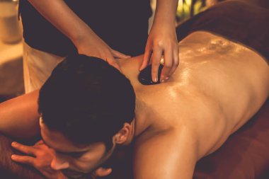 Sıcak mum ışığıyla lüks bir tatil köyündeki kaplıca salonunda sıcak taş masajı, mutlu erkek müşteri bazalt taşı masajının keyfini çıkarırken rahatlatıcı bir sıcaklıkla vücudun üzerinde süzülüyor. Sessiz.