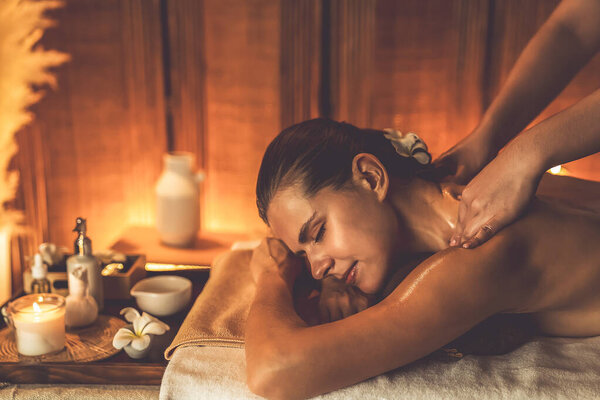 Caucasian woman customer enjoying relaxing anti-stress spa massage and pampering with beauty skin recreation leisure in warm candle lighting ambient salon spa at luxury resort or hotel. Quiescent