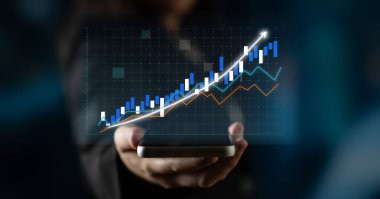 Bir işadamı, yükselen eğilimli dijital grafik gösteren bir akıllı telefon tutuyor. Bu görüntü finansal başarının ve iş dünyasındaki veri odaklı analizin özünü yakalar. Etki