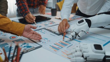 Bir konferans masasında insan ve robot ellerinin veri grafikleriyle meşgul olduğu, iş dünyasındaki işbirliğinin ve yeniliğin geleceğini simgeleyen dinamik bir toplantı sahnesi. Noogenesis