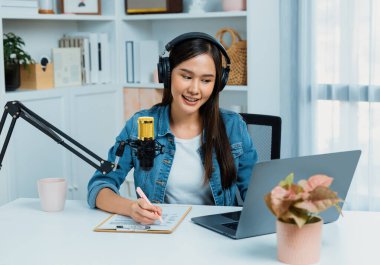 Sosyal medyada kulaklıkla canlı yayın yapan Asyalı sunucu modern stüdyoda yaşam koçluğu veya pazarlama dinleyicilerini selamlıyor. Taktik.