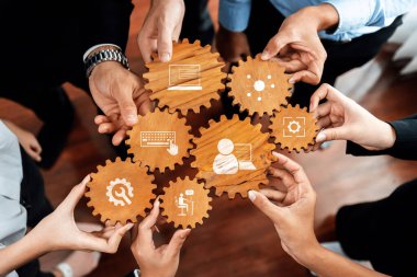 Bu resim, modern ofis ortamında takım çalışmasını ve yenilikçi fikirleri sembolize eden ahşap dişlileri tutan bir işbirliği çabası sergiliyor. Dostluk