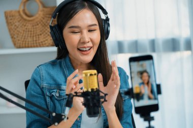 Asyalı sunucu canlı yayında canlı yayında canlı yayında sosyal medyada kulaklık takarak konuşuyor. Dinleyicileri modern stüdyoda koçluk yaparak selamlıyor. Taktik.