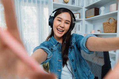 Sunucu kanalı genç ve güzel Asyalı kız akıllı telefonuyla selfie çekiyor. Modern stüdyo ofis konseptinde kulaklık takıyor. Sahne arkası yayıncısı sosyal medyada canlı yayın yapıyor. Taktik.