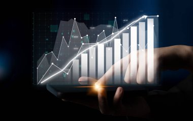 Bir el, karmaşık veri görsellemelerini gösteren, modern bir iş ortamında grafik ve grafikleri gösteren dijital bir tabletle etkileşir. Etki