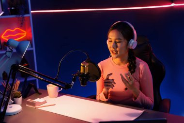 Geceleri podcast 'te olumlu konuşmalar yapan, pembe neon ışıklı modern stüdyoda sunum için dizüstü bilgisayar kullanan, gülümseyen, genç, güzel Asyalı bir etkileyiciydi. Taktik.