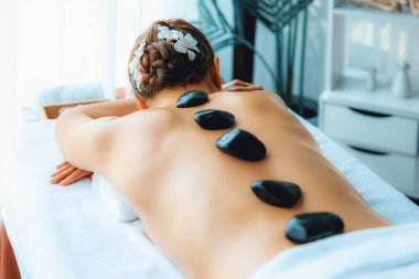 Lüks tatil köyündeki kaplıcalarda sıcak taş masajı. Gün ışığı sükunet ortamında, mutlu kadın müşteri bazalt taş masajından zevk alıyor. Rahatlatıcı bir sıcaklıkla vücudun üzerinde süzülüyor. Sessiz.