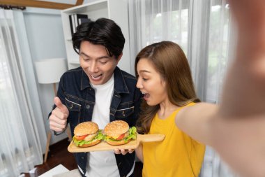 Gülümseyen sunucu şefler akıllı telefonlarıyla fotoğraf çekiyorlar. Özçekim yoluyla. Yemek programında çift hamburger tutuyorlar. İnfobahn.