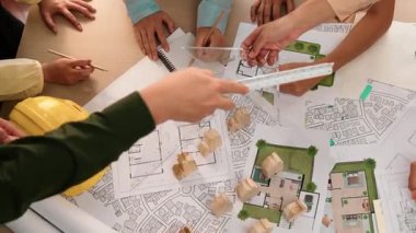 Mimari belge, ölçüm aracı ve ahşap blokların modern ofiste etrafa saçıldığı bir masa üzerinde yapı inşaatı ile ilgili mimar ve güvenlik mühendisi tartışması. Tanımlama.