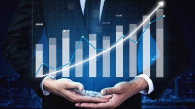 Takım elbiseli bir işadamı, geceleri çağdaş bir şehir siluetine karşı yatırımlarda yükselen bir eğilimi gösteren parlak bir mali büyüme tablosu sunuyor. Copula