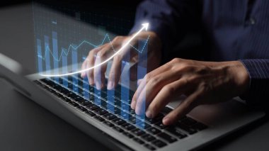 Bilgisayarda yazı yazan ellerin yakın plan görüntüsü, grafiklerin dinamik dijital veri görselleştirmesini gösteren, finansal büyümeyi ve iş analitiğini sembolize eden. Copula