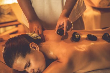 Lüks tatil köyündeki kaplıcalarda sıcak taş masajı, sıcak mum ışığı, spa bazalt taşı masajının keyfini çıkaran mutlu kadın müşteriler, rahatlatıcı bir sıcaklıkla vücudun üzerinde süzülüyorlar. Sessiz.