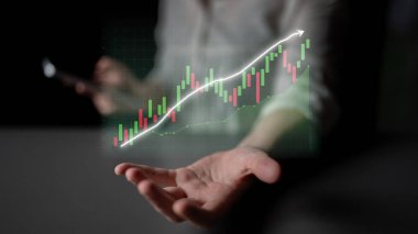 Bir erkek el, modern teknoloji ve iş analizlerindeki büyüme ve başarıyı gösteren, yükselen bir eğilimle holografik bir finans tablosunu gösteren bir akıllı telefon sunar. Etki