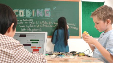 Kafkas arkadaşı STEM sınıfında elektrik panosunu tamir ederken Asyalı çocuk kodlama programı. Enerjik öğrenci kodlama mühendisliği komut yazarken ve yapay zeka yazılımını programlarken tahtada duruyor. Pedagoji.