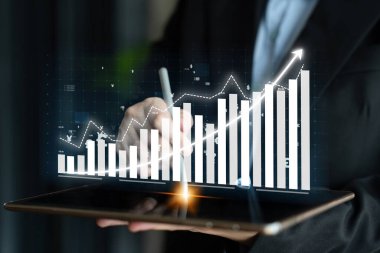 Bir iş adamı, görsel grafikler ve grafiklerle verileri analiz etmek, finansal büyüme ve modern analitik teknikleri sergilemek için tablet kullanır. Etki
