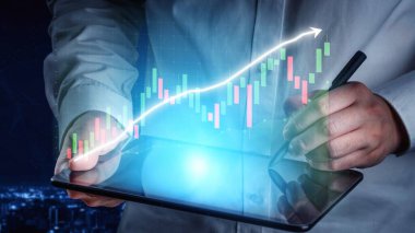 Bir iş adamı finansal verileri analiz etmek için tablet kullanır, geceleri modern bir ofiste büyüyen bir tabloyla borsa eğilimlerini sergiler. Copula