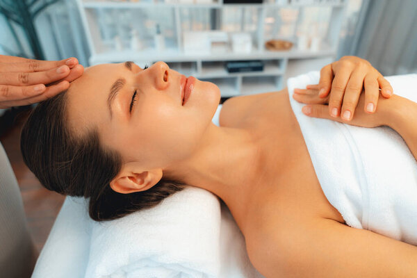 Caucasian woman enjoying relaxing anti-stress head massage and pampering facial beauty skin recreation leisure in dayspa modern light ambient at luxury resort or hotel spa salon. Quiescent