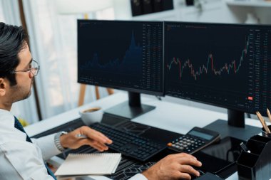 Akıllı tüccar işadamı, modern merkez ofisindeki araştırma pazarında en yüksek kârlı finansal teknolojiye yatırım yaparak bilgisayar üzerinde iki dinamik borsa yatırım ekranını analiz ediyor. Tahmin et..