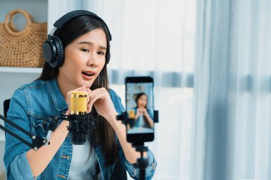 Asyalı sunucu canlı yayında canlı yayında canlı yayında sosyal medyada kulaklık takarak konuşuyor. Dinleyicileri modern stüdyoda koçluk yaparak selamlıyor. Taktik.