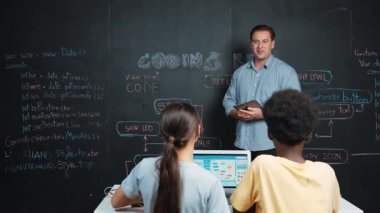 Kodlama programıyla ilgili öğrenci sorusuna beyaz öğretmen cevap veriyor. Beyaz kız, STEM teknoloji sınıfında dizüstü bilgisayar ekranı görüntülerken soru sormak, oy vermek, gönüllü olmak için elini kaldırdı. Öğretim