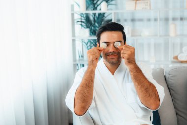 Elinde taze salatalık dilimleri tutan ve bornoz giyen bir adam tatil köyünde ya da otelde yüz bakımının keyfini çıkarıyor. Yüz ve güzellik tedavisi için cilt bakımı. Sessiz.