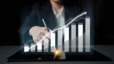 Bir işadamı, dijital grafik ve grafikleri gösteren modern bir tablet kullanarak finansal verileri analiz eder, profesyonel bir çevrede büyüme ve stratejiyi vurgular. Etki