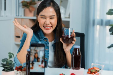 Gülümseyen, güzel Asyalı genç, lezzetli karışık çilek ve kiraz suyu detoksu içeceklerini inceleyen, sosyal medyada özel promosyon satışı için sağlıklı ürünler sergileyen. Taktik.
