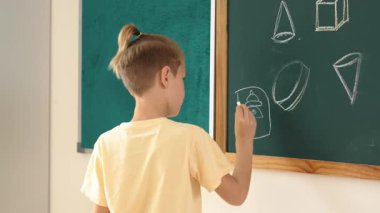 Kafkasyalı enerjik zeki çocuk sınıfta tahtada dururken hayal gücünü ifade etmek ve geliştirmek için resim çiziyor. Sanat dersinde karatahtaya yazı yazan çekici ilkokul öğrencisi. Pedagoji.