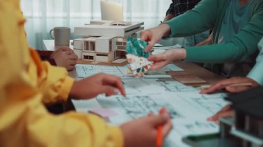 Çeşitli bir ekip modern bir ofiste, çeşitli araç ve belgelerle mimari tasarım ve proje planlarını tartışan bir ortak toplantıya katılıyor. SACTR