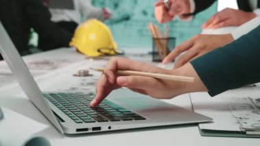 Profesyoneller, modern bir ofiste dizüstü bilgisayarlar ve planlar kullanarak bir inşaat projesinde işbirliği yapıyorlar. Çevre, yenilikleri ve takım çalışmasını teşvik eder, aktif planlamayı ön plana çıkarır. SACTR