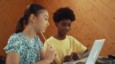 Afrika 'lı bir erkek ve beyaz bir kızın günlük giysiler içinde BTMM teknoloji sınıfında dizüstü bilgisayar ve elektronik ekipmanlarla kod yazma ya da programlama sisteminde birlikte çalıştıklarını gösteren site görüntüsü. Öğretim