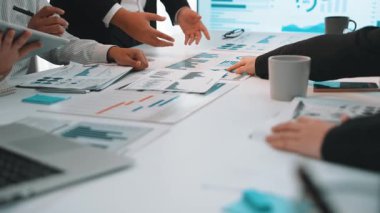 Modern bir ofis ortamında, çizelgeler ve dizüstü bilgisayarlar üzerinde işbirliği yapan profesyonellerin yer aldığı, veri analizi ve stratejik tartışmaların vurgulandığı dinamik bir iş toplantısı. SACTR